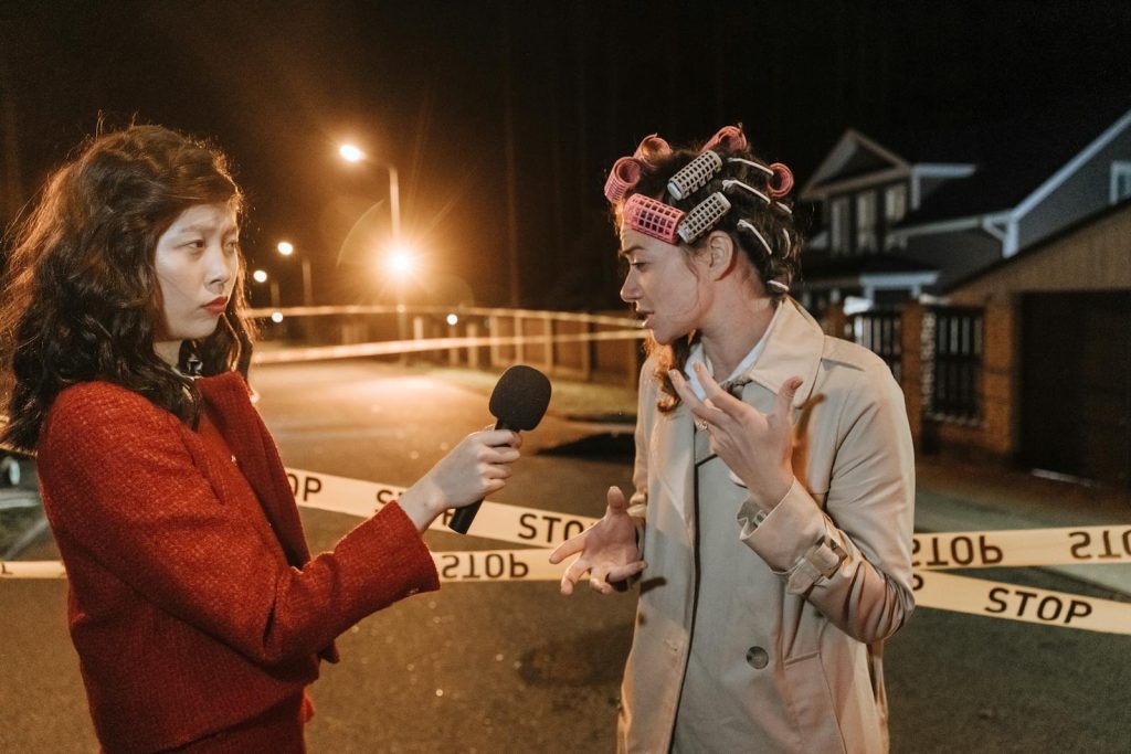 What's the Difference Between Campus Journalism and Actual Journalism in Newspaper Companies? 6 Asian female journalist interviews a woman at a night crime scene. Police tape marks the area.