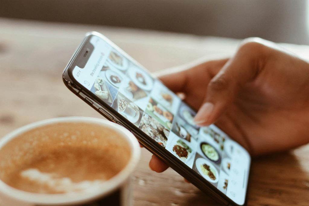 5 Resources to Develop Digital Citizenship, and the Mistakes Other Netizens Do 6 Hand browsing social media photos on a smartphone next to a cup of coffee indoors.