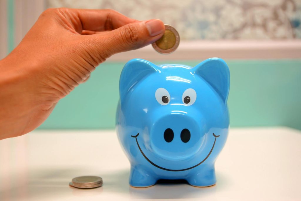 Son Gives First Salary to Mother, but His Mother Did Not Accept It. Why? 6 Hand inserting a coin into a blue piggy bank for savings and money management.