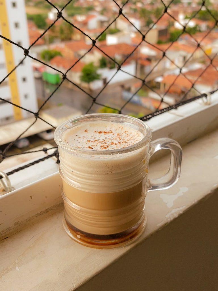 Learn How Feynman Technique Unlocks Your Greatness to Thump Complex Concepts 8 A frothy latte in a glass mug on an urban window sill with a city view background.