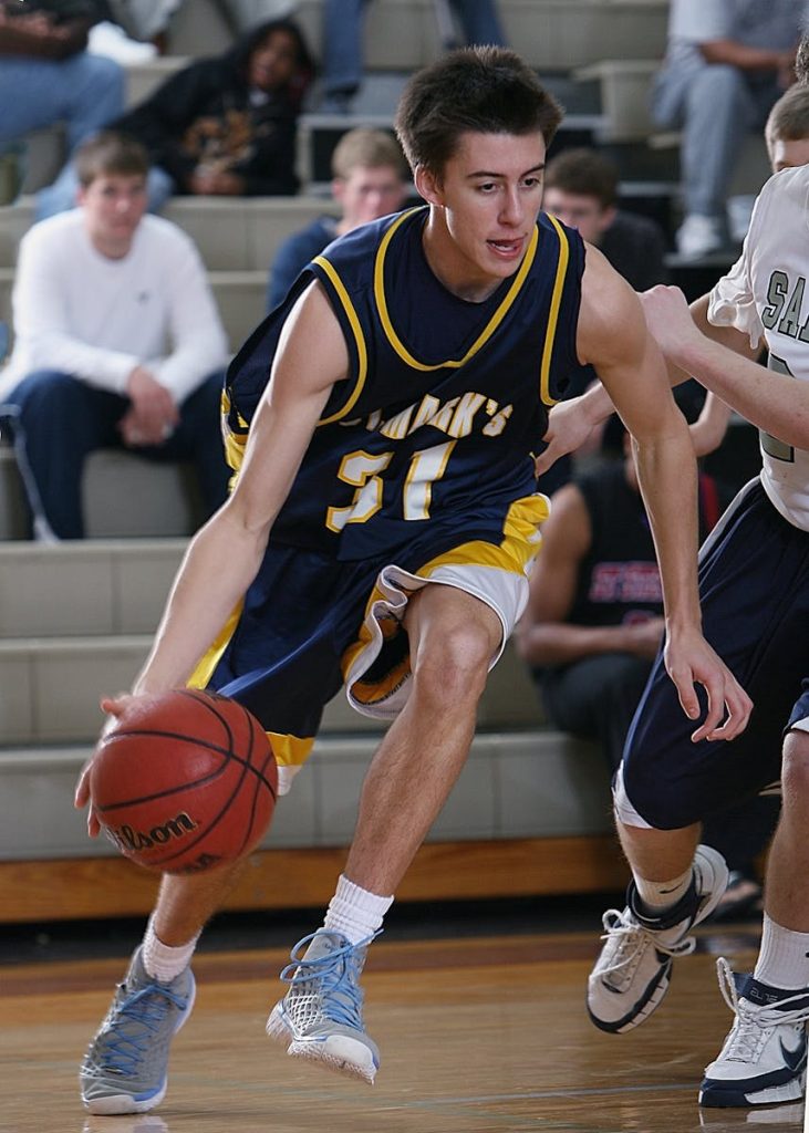 Teen basketball player dribbling during an intense game in a school gym.