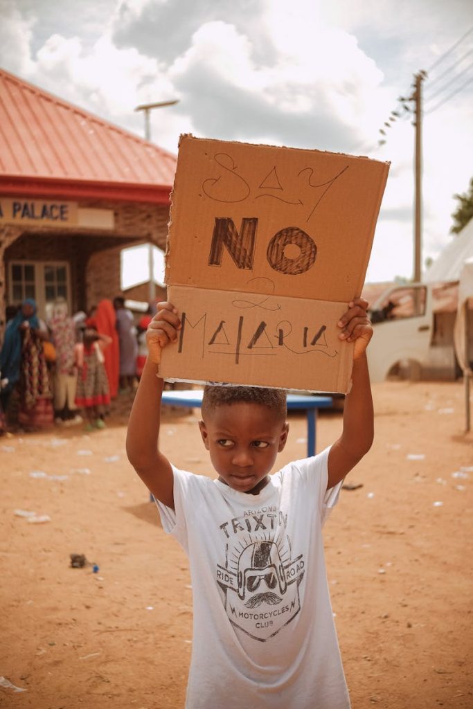 Young child holding a sign against malaria outside in Nigeria.