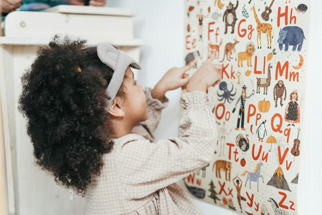 10 No Nonsense Classroom Management Strategies for Preschool Learners in the Digital Age 8 Child with curly hair points to an animal alphabet poster indoors, learning letters and animals.