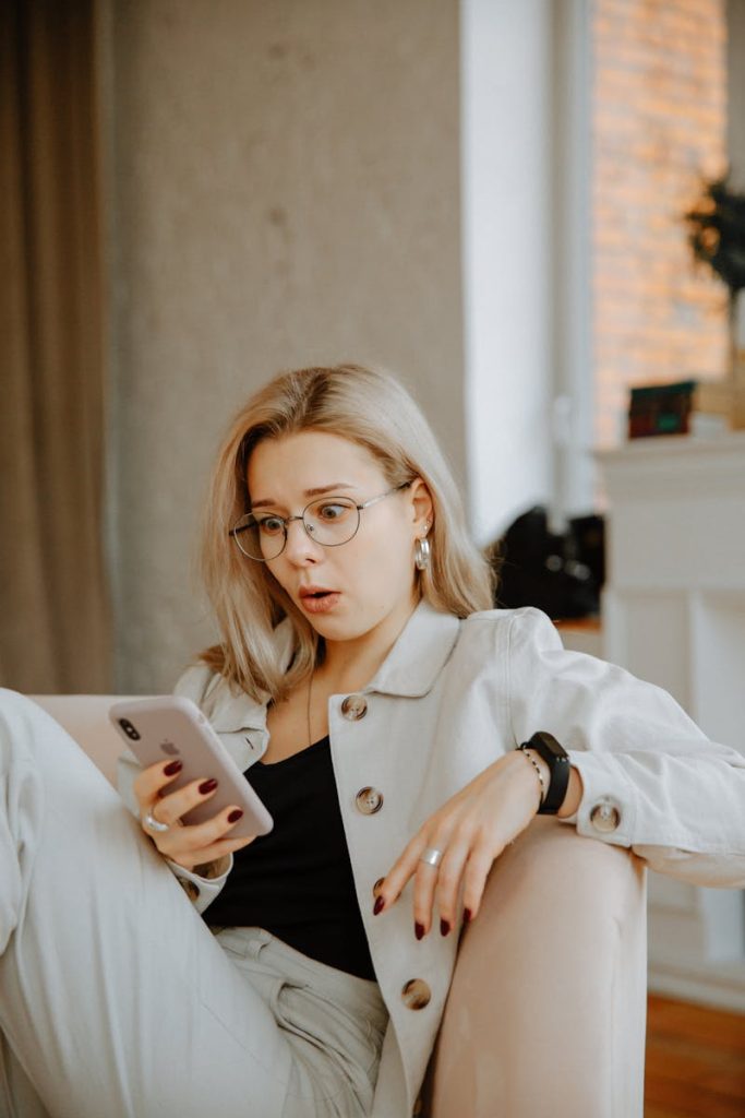 6 Helpful Stratagem for Effective Mobile Journalism Reporting 7 Surprised woman with glasses reacts to news on her phone while relaxing indoors.