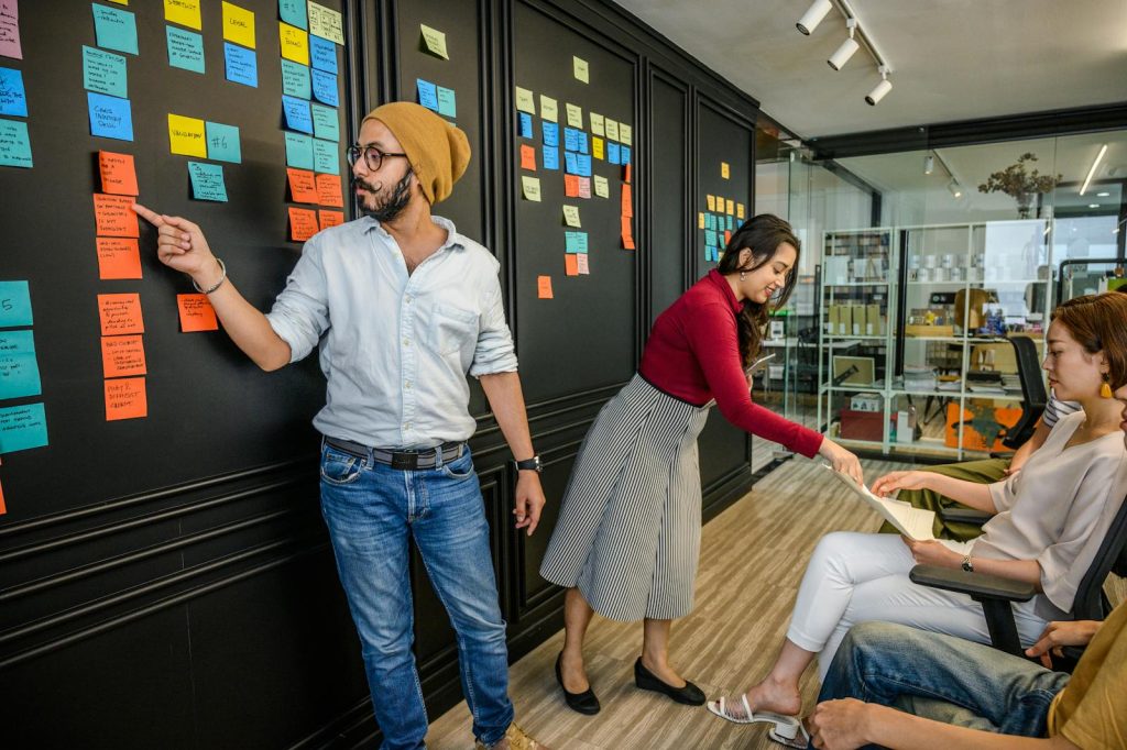 Here's 6 Ways to Develop Student Hotshot By Utilizing Thought-Provoking Discussions 6 Team members collaborating in a modern office with sticky notes on a wall, focusing on brainstorming and strategy.