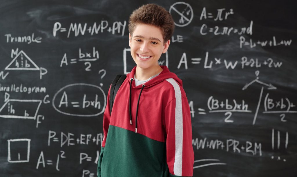 Problem with Classroom Management for Junior High School? Here's How to 10 Techniques to Fix It 7 Smiling student in a classroom posing in front of a chalkboard filled with math formulas.