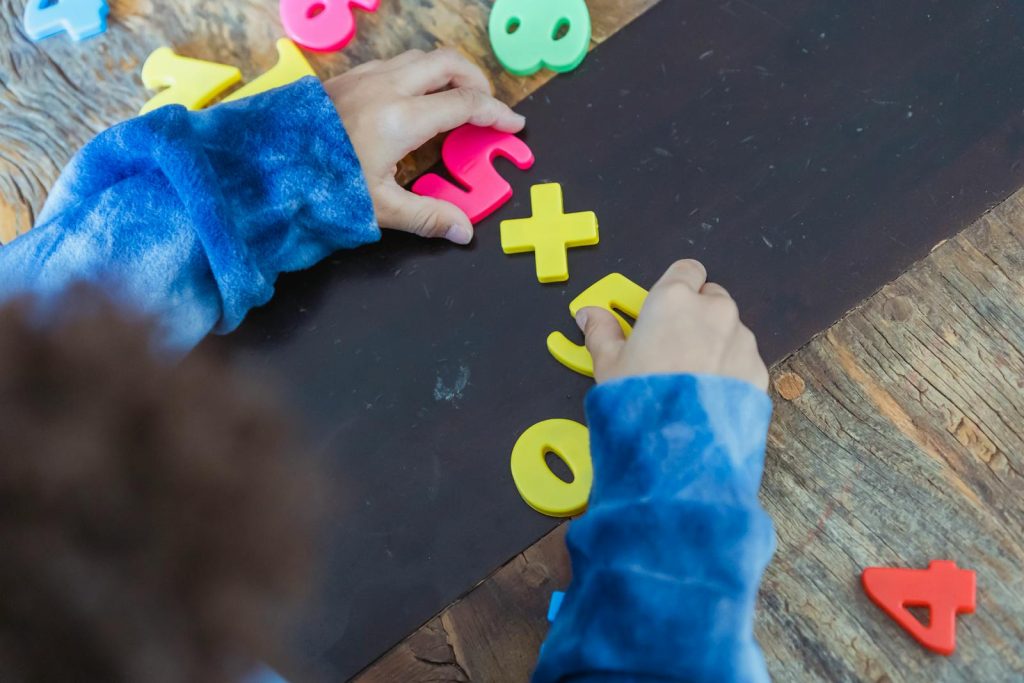 7 Turbo-charge Advantages of Learning Lessons and Topics Through Games, and Why We Recommend It 7 A child playing with colorful number magnets on a wooden table, promoting early education.