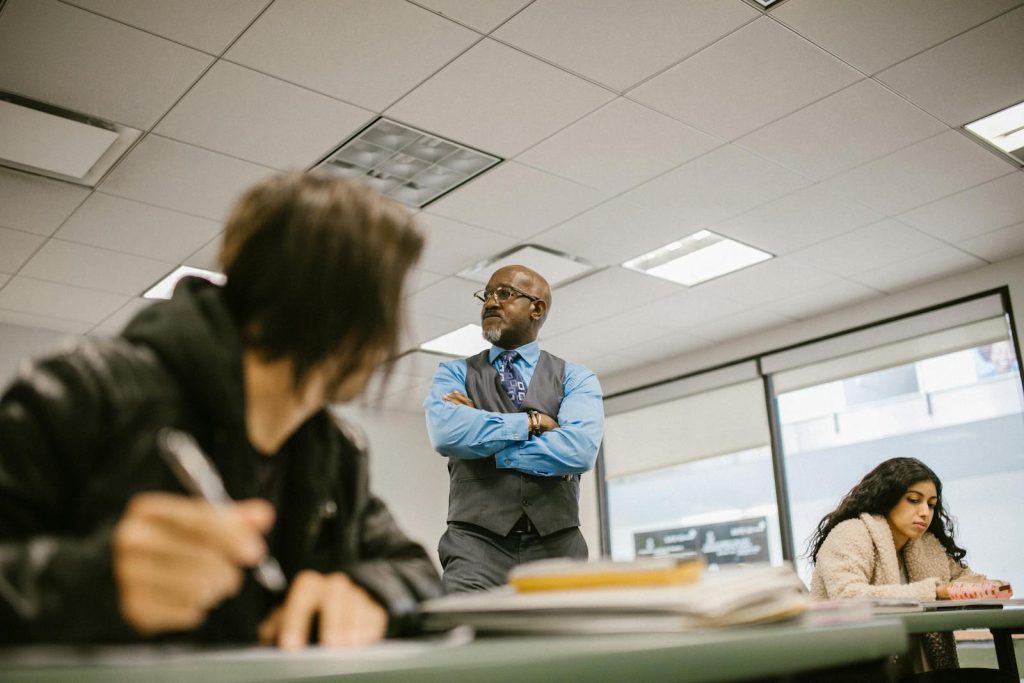 9 Indubitable Tactics to Pass College Entrance Exam Like a Maven 8 A professor attentively watches students during an exam in a college classroom setting.