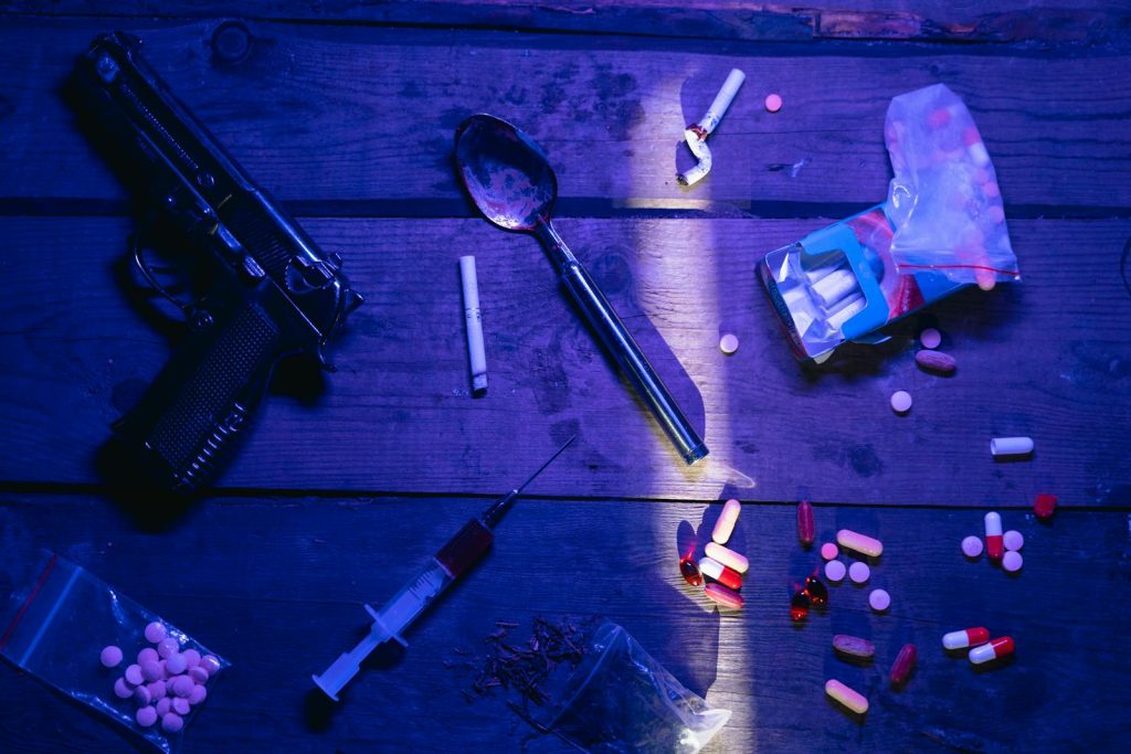 10 Brutal Strategy to Slay Writing Crime-Related News Article for Bootleg Output 9 Intriguing still life image depicting pills, a gun, and syringe under dramatic lighting.