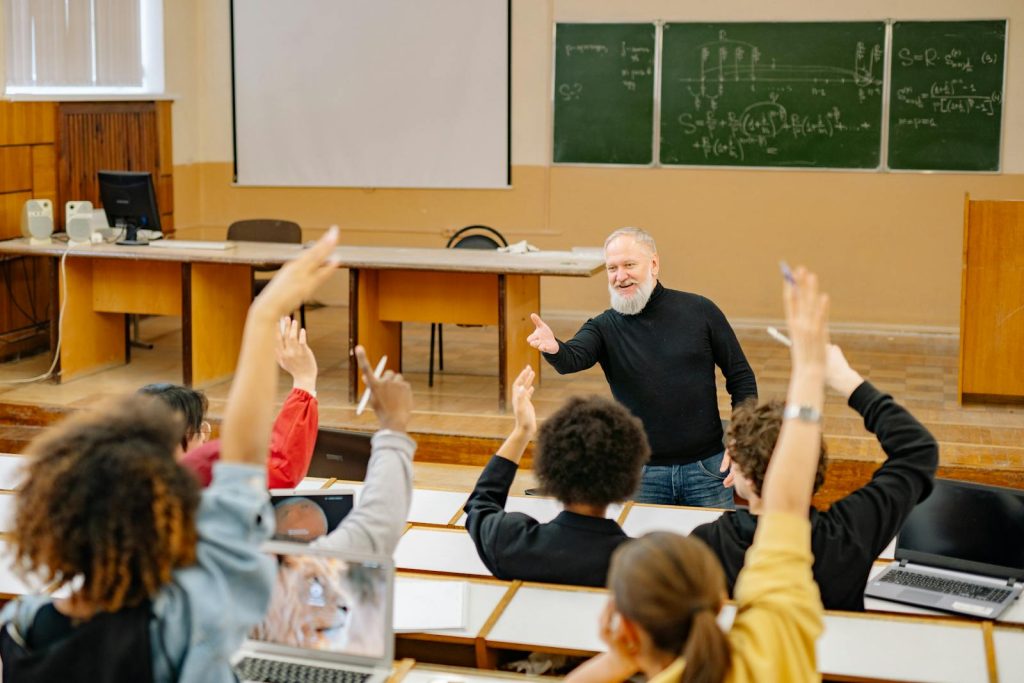 5 Supreme Techniques for Effective Questioning and How to Apply it in Class Like a Pro 7 Professor engaging with students in a lively university classroom discussion as students raise hands.