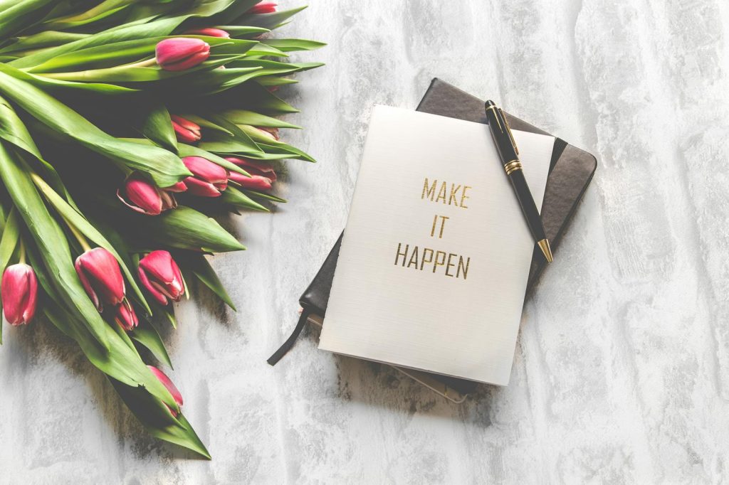 10 Often Underused Yet Effective Tips to Develop an Unparalleled and Effective Note-Taking Strategy 6 A notebook with 'Make It Happen' inscription beside a bouquet of pink tulips, capturing inspiration.