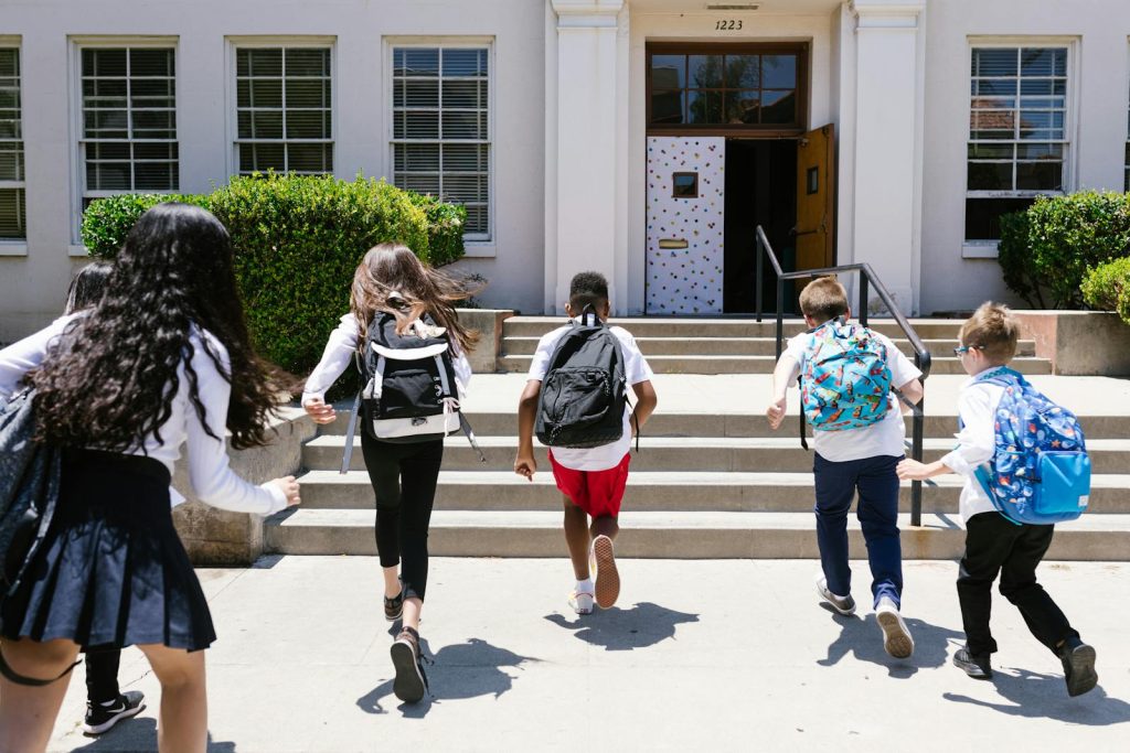 10 Simple Things to Soar Results with Classroom Management for Middle School Learners in the Digital Era 7 Group of students with backpacks running into school, captured from behind, showing excitement.