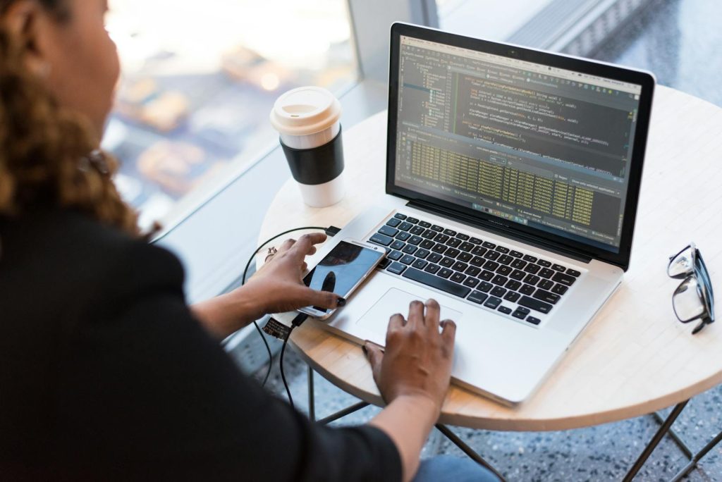 Top 10 Insanely High-Paying Careers in the Philippines - For Your Career Guidance 6 Black woman programming on a laptop with coffee, smartphone, and glasses on a desk in an office.