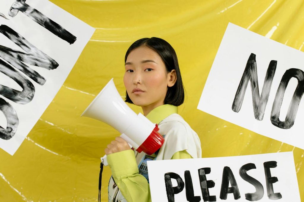 9 Incredibly Great Column Writing Tips to Produce a Noteworthy Article 8 Portrait of a young activist holding a megaphone against a yellow background surrounded by protest signs.