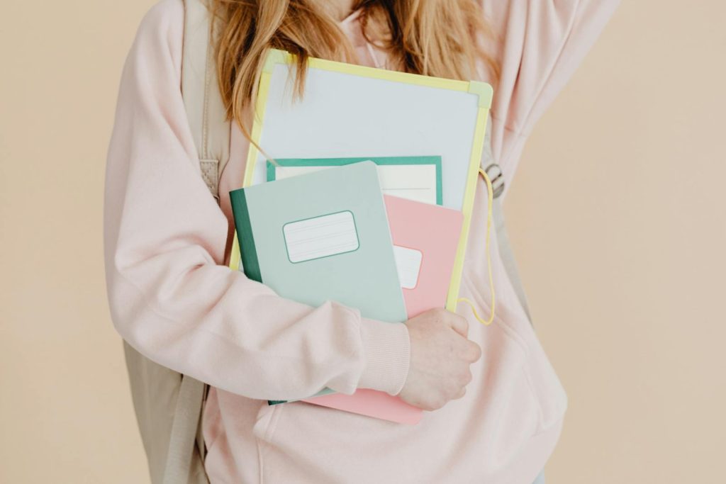 4 Steps to Incorporate Spaced Repetition in Study Routine - Learn Strategically Thru Spacing Effect 5 Young student in pink hoodie holding colorful notebooks, ready for school.
