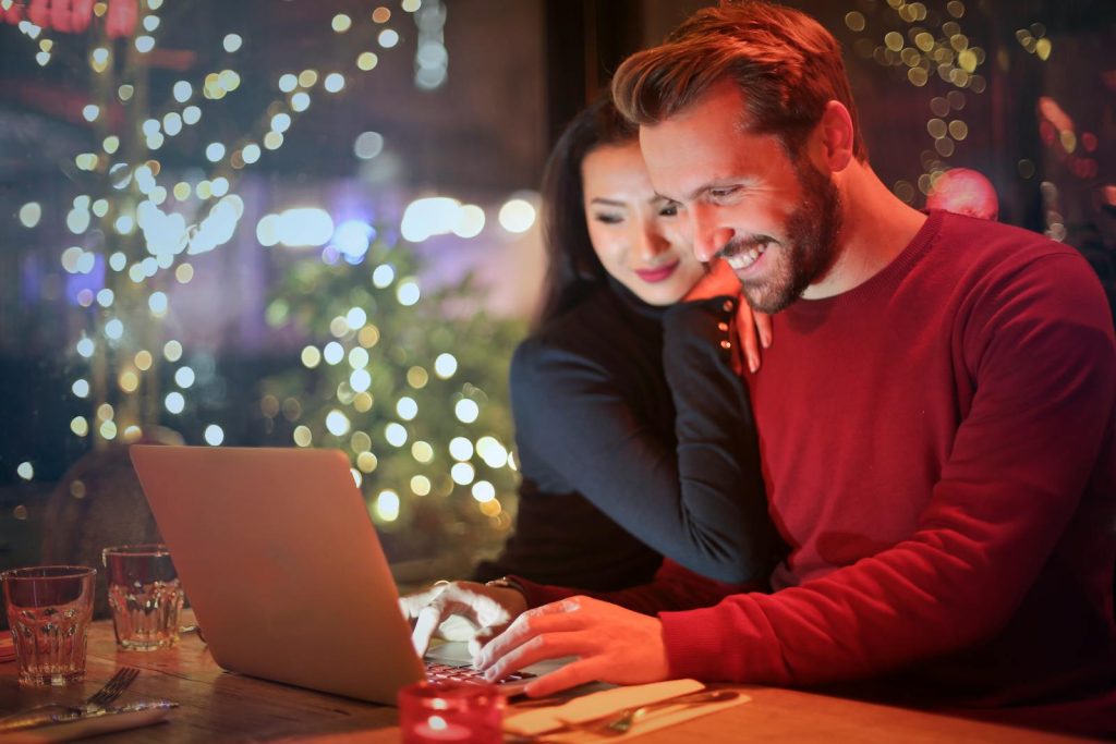 The Complete Guide to Understanding 5G Technology + Advantages and Concerns 5 A couple using a laptop at a cozy restaurant with festive bokeh lights, enjoying online shopping together.