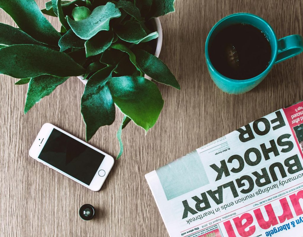 10 Tips Turn Yourself into a Sterling News Writer at Press Conferences 8 Flat lay arrangement of a coffee mug, newspaper, smartphone, and plant on a wooden table.