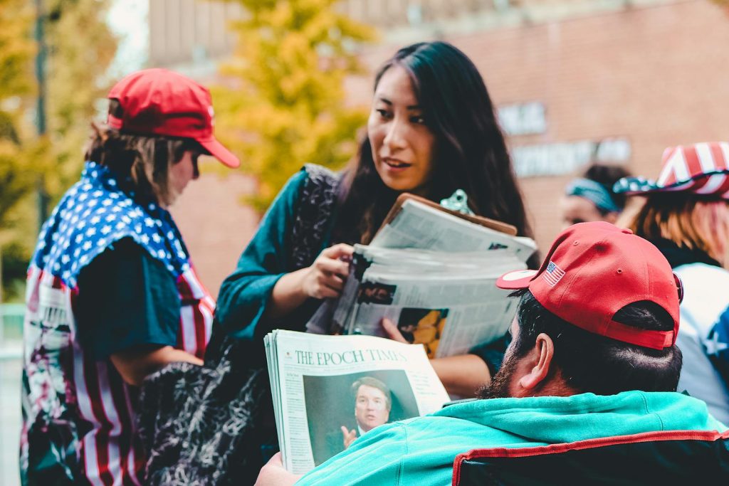 How to Become a Great Editorial Writer, A Tip from an NSPC Qualifier 5 A group of adults reading newspapers outdoors, immersed in political discussions on a vibrant day.