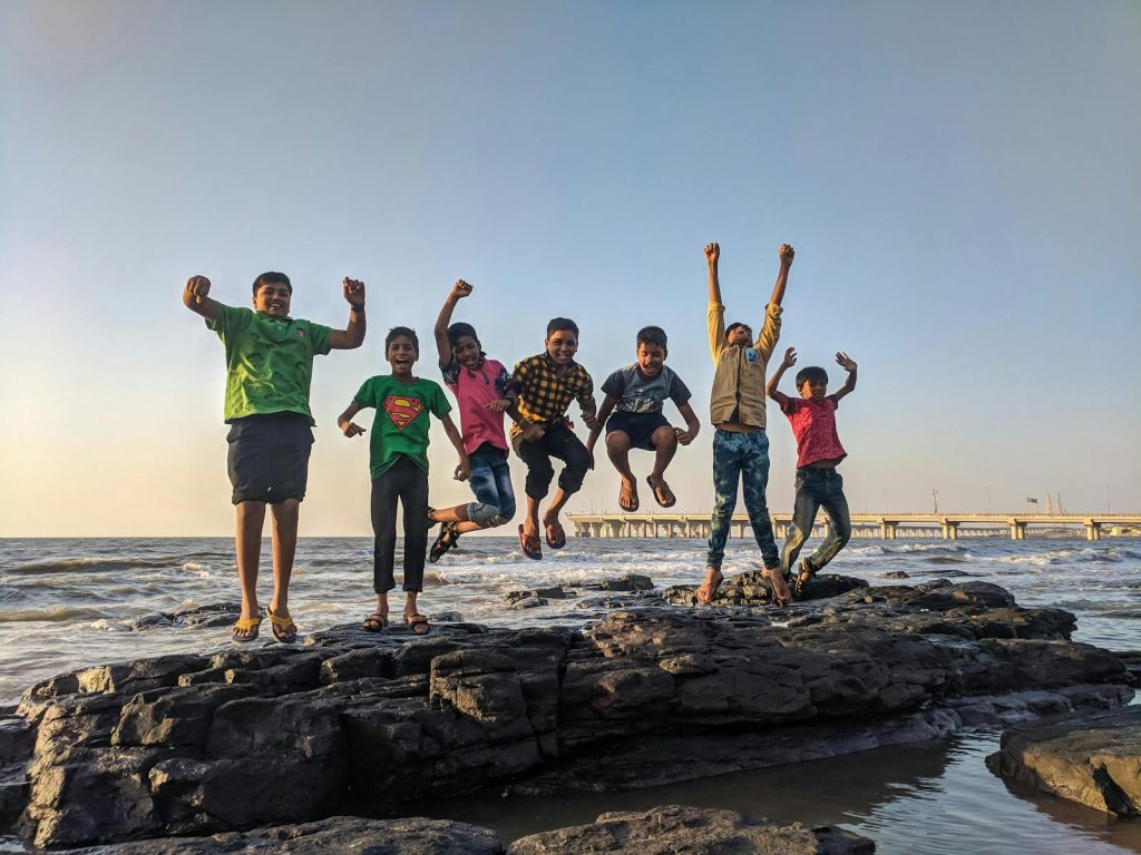 DepEd Launches Telesafe Program to Celebrate National Children's Month - Masugpo ang Pang-aabuso 6 Group of kids joyfully jumping on rocks by the seaside. Fun and playful moment captured outdoors.