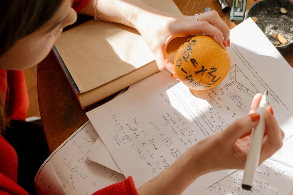 6 Secrets to Study Effectively and Easily Make an Outstanding Performance in Long Test 6 Student studying math creatively using an orange and notes in warm indoor light.