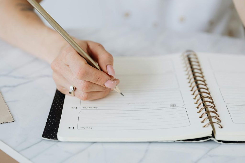 4 Stunning Note-Taking Methods That Will Help You Understand Information More Effectively 7 Close-up of a woman's hand writing in a spiral notebook on a marble desk.
