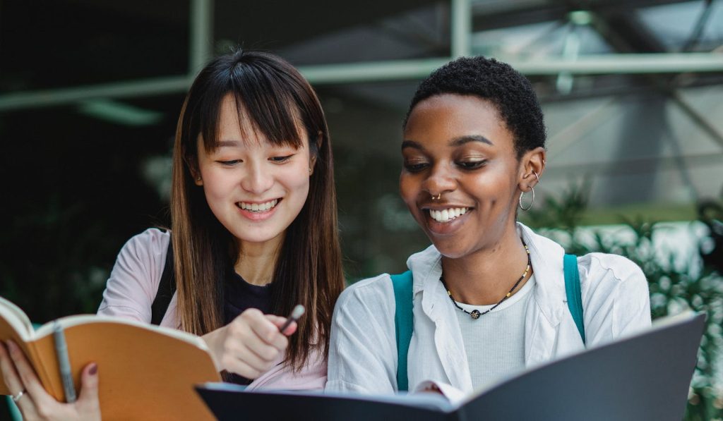 Two happy ethnic students enjoying studying together outdoors, showcasing diversity.