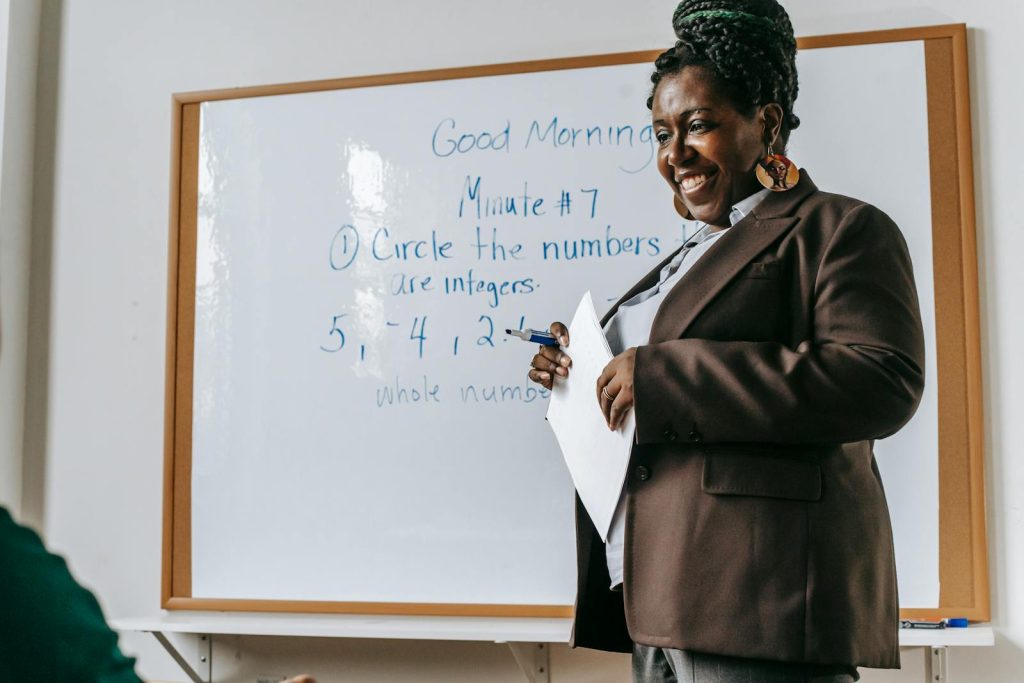 4 Easy Steps to Utilize Self-Explanation, Effective Strategy to Make Sense of New Information & Deeper Understanding 7 Crop smiling African American female teacher standing near whiteboard with papers in hands during math lesson