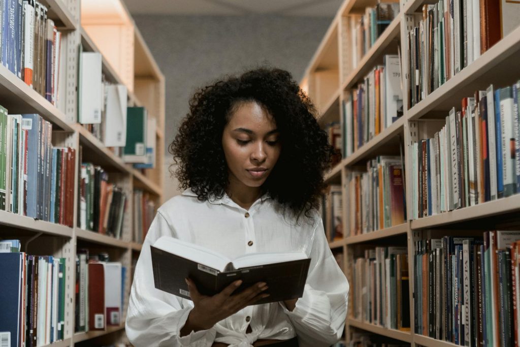Couple in Bohol Has 59 Scholars - Provides Them School Supplies, Laptops, Cellphones, Printers, Others 5 African American woman with curly hair standing in a library reading a book.