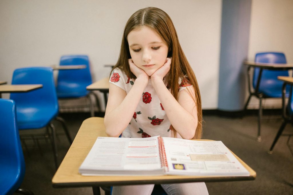 Heavy Workload and Excessive School Decorations Lead to Poor Student Performance in the Philippines? 6 A young girl sits thoughtfully at her desk in a classroom, reading a textbook.