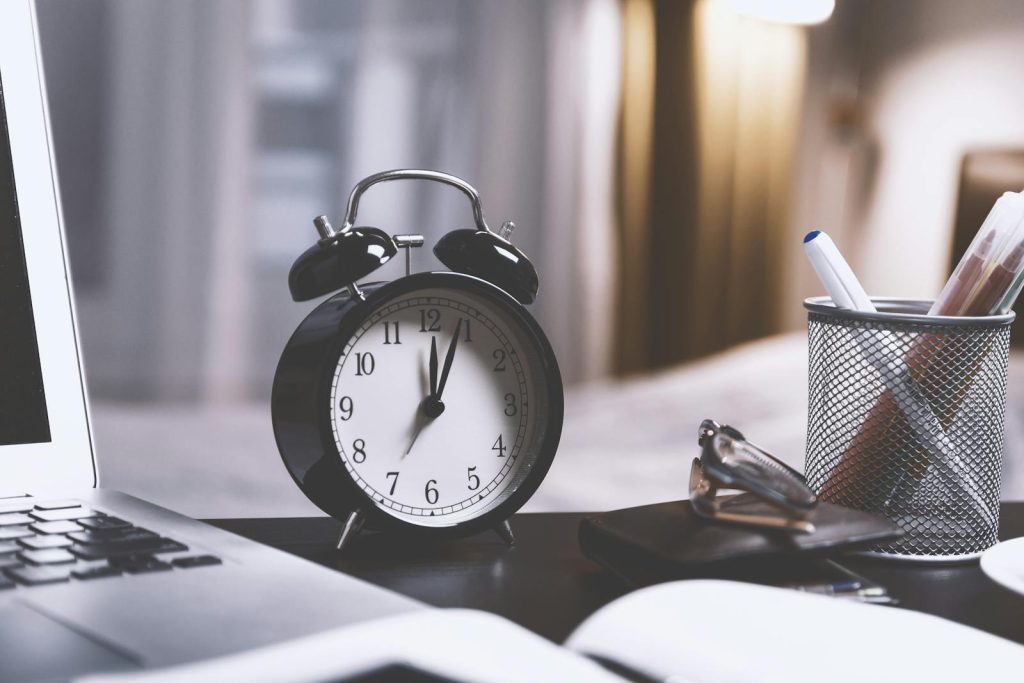 5 Easy Steps to Using the Pomodoro Technique, Game-Changing Tool For Procrastinators 5 A classic analog alarm clock on a modern desk setup with a laptop and pens, creating a balanced workspace vibe.