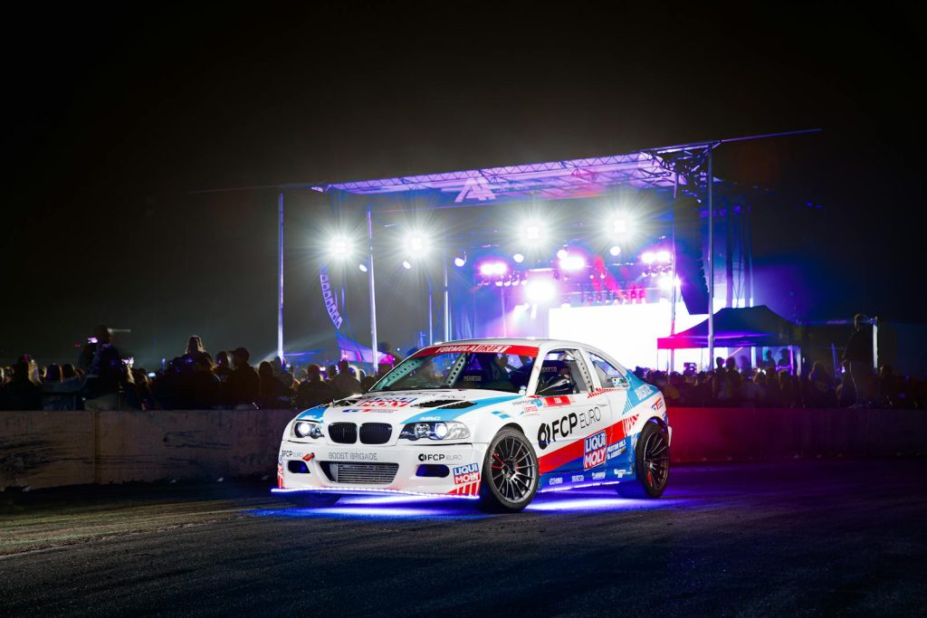 Exciting nighttime car racing event featuring a driver and illuminated race car on a track.